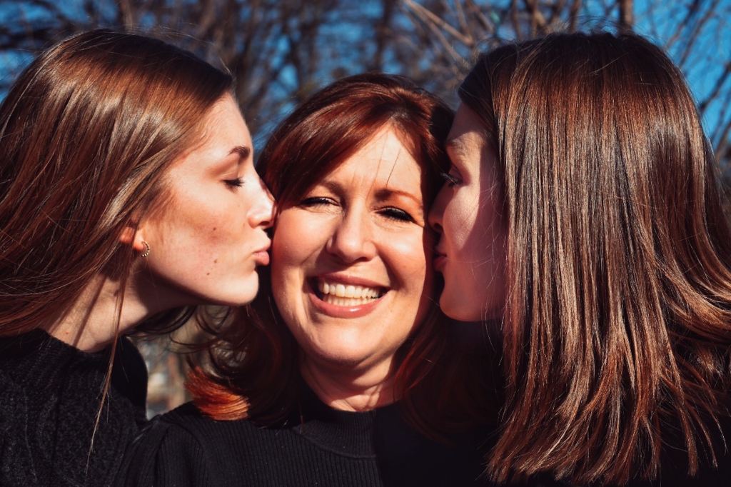 Mother stands between daughters who kiss her cheeks.